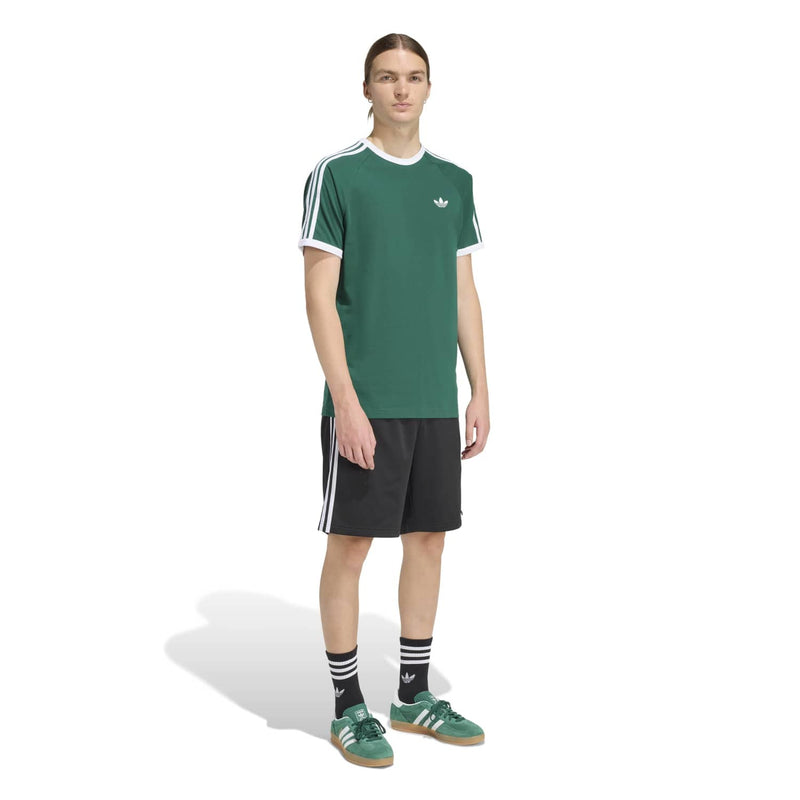 Men's green t-shirt worn with black athletic shorts; white three-stripe sleeve detailing