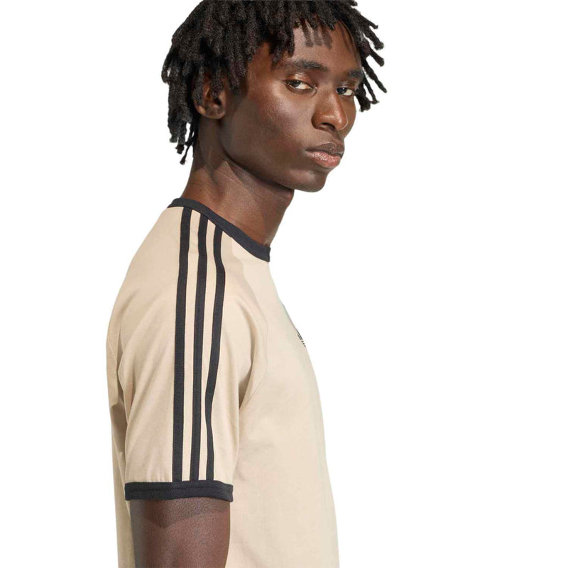 Side view stone khaki tee with black shoulder stripes and collar trim, small chest trefoil