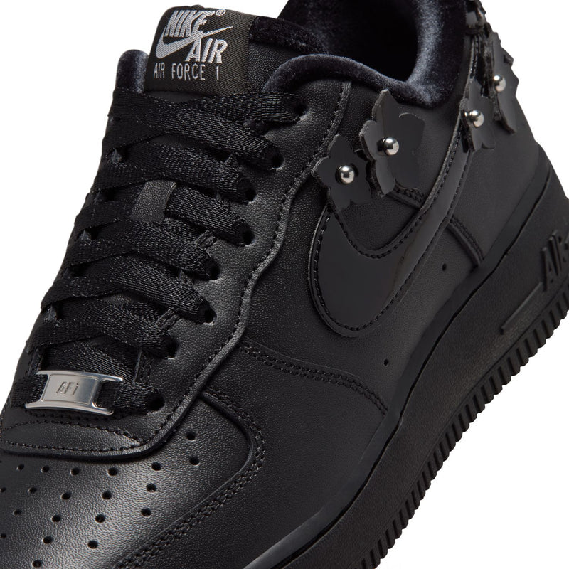 Women's black low-top sneaker close-up of laces and studded ankle charm details