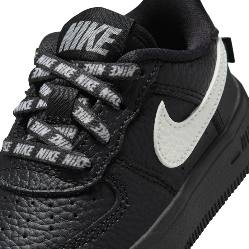Close-up of black toddler sneaker with white swoosh and printed lace loops