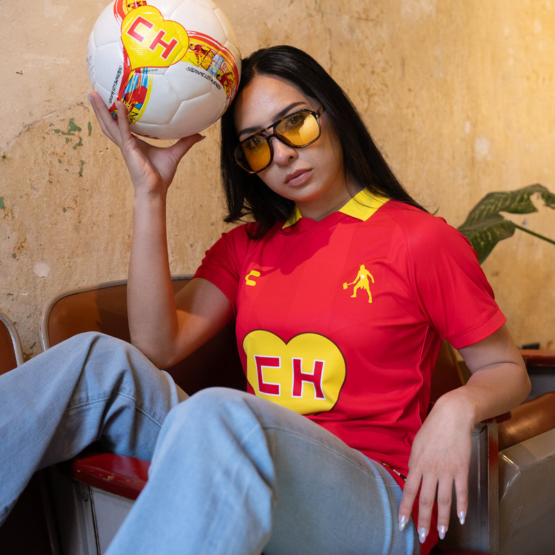 Red men's soccer jersey with yellow collar and EH heart logo, worn by model