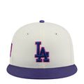 Two-tone baseball cap, cream crown with purple brim and blue/pink LA logo.
