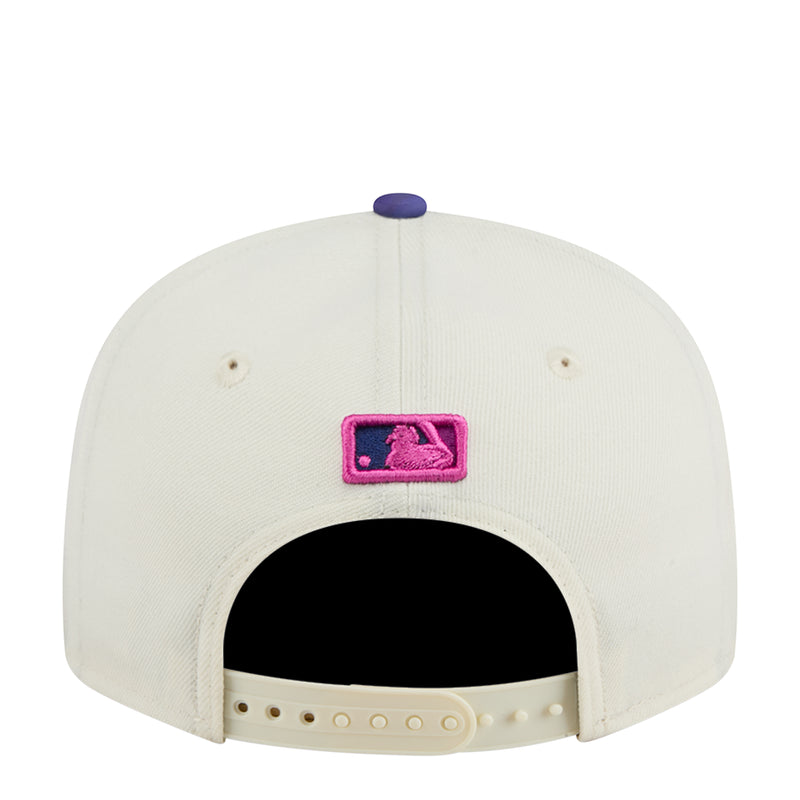 Two-tone baseball cap with cream front, pink emblem, black interior and snapback strap.