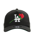 Black A-frame baseball cap with white LA logo, red rose patch, and green stem embroidery