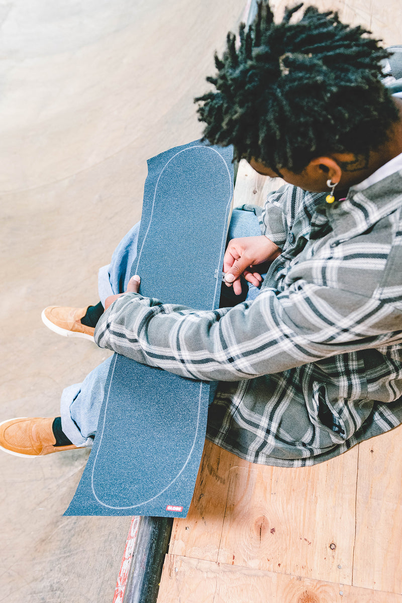 Person with plaid shirt sitting on a ramp holding a blue skateboard deck