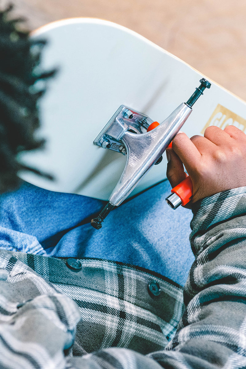 Close up of a silver skateboard truck being tightened with a T-tool on a light blue deck