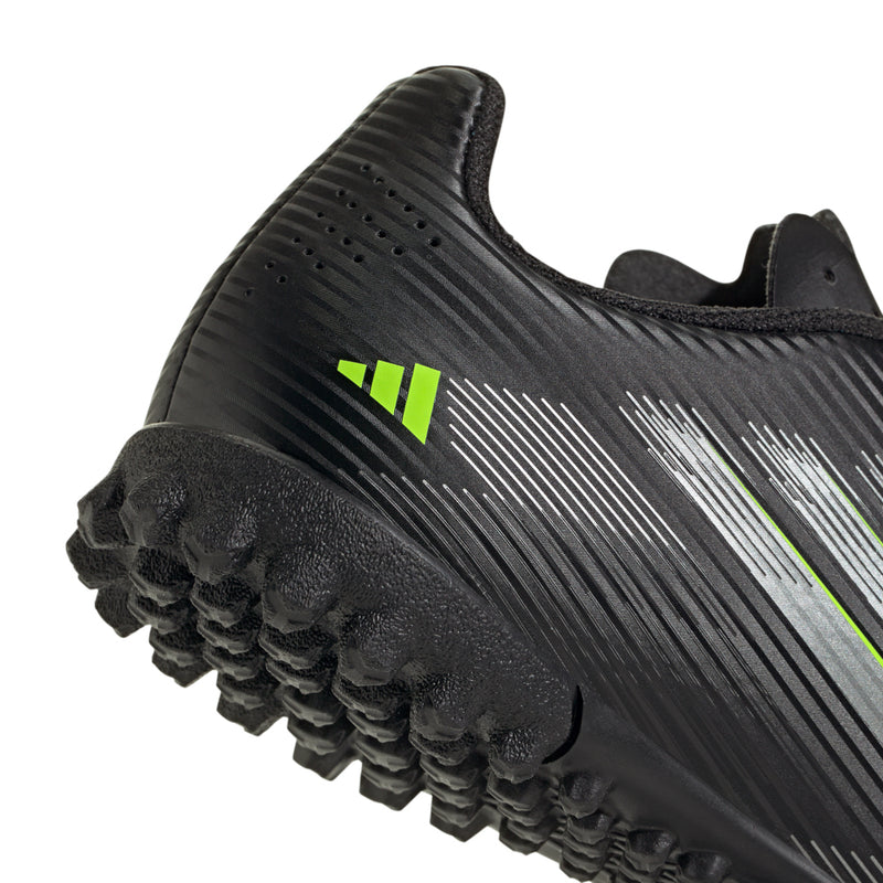 Youth black soccer cleat toe: textured stripes, neon green mark, and raised rubber studs
