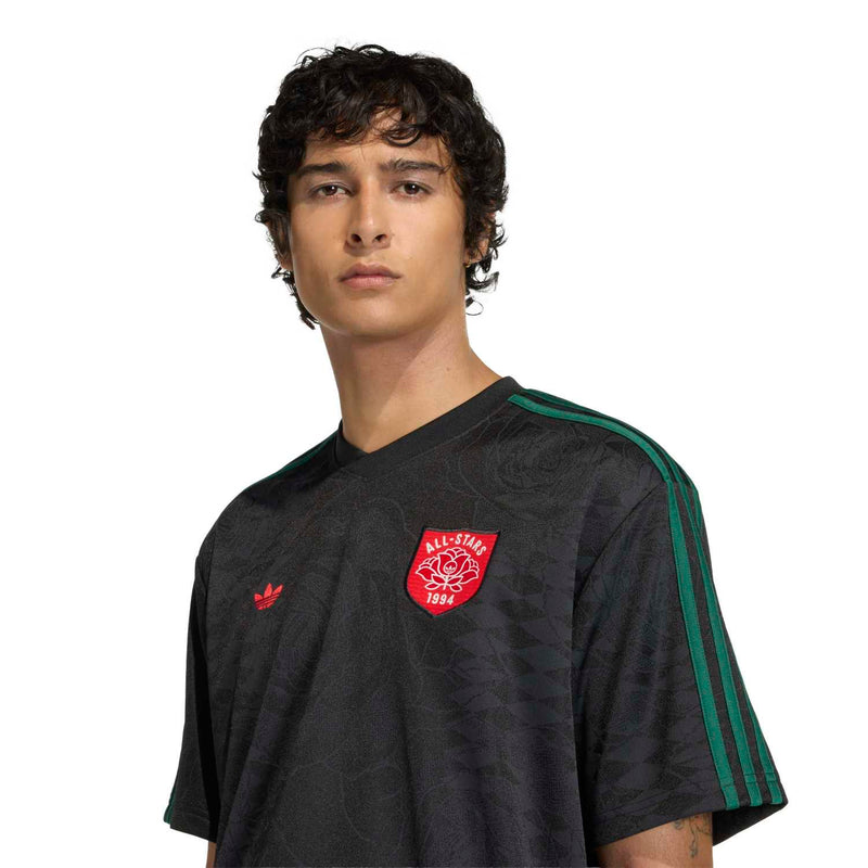 Men's black football jersey close-up: red crest logo and green sleeve stripe