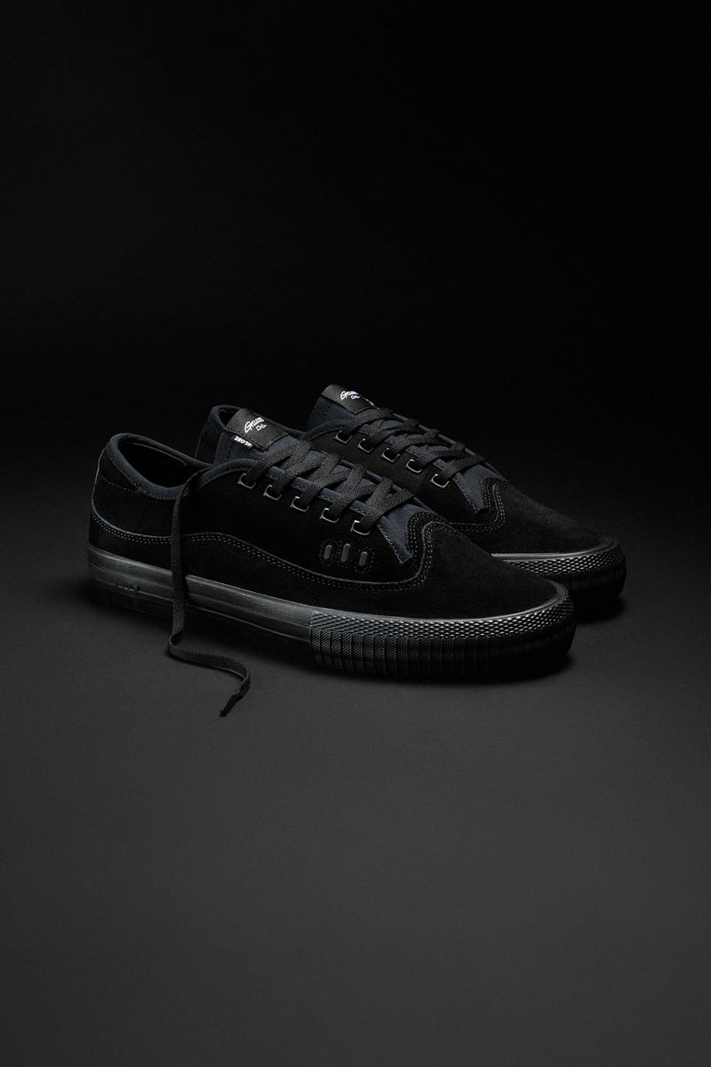 Gillette black suede sneakers with textured black sole on dark studio background.
