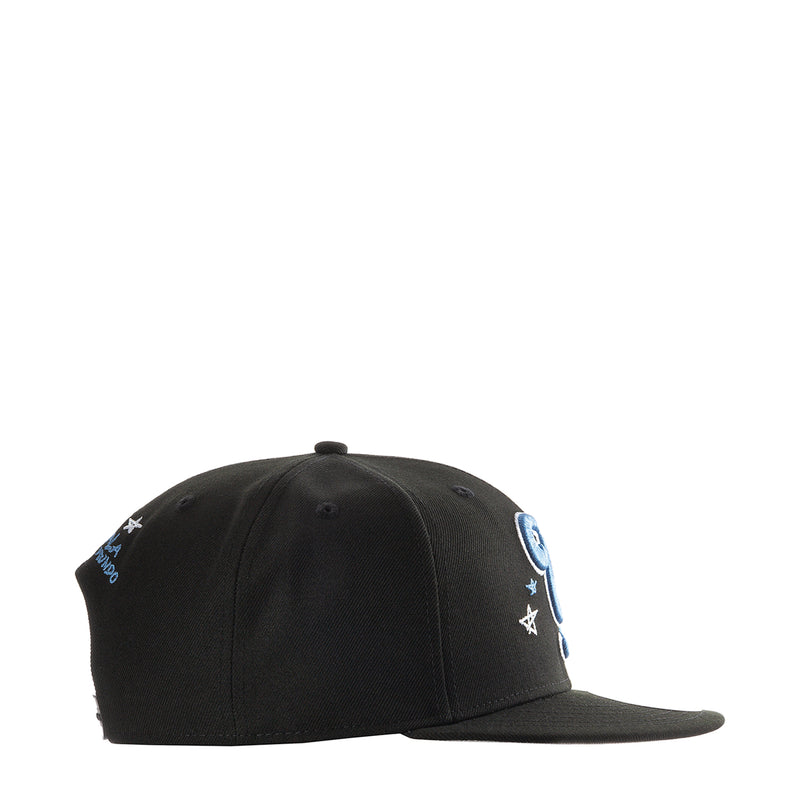 Black baseball cap with small blue side patches and star accents along the crown