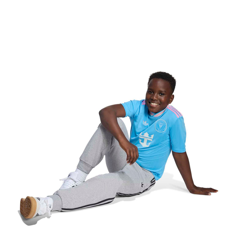 Youth light-blue soccer jersey with team crest and anchor logo, worn by model seated