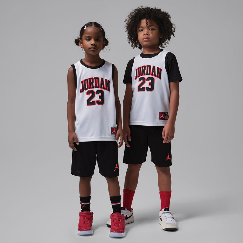 Kids basketball set on model: white jersey with red Jordan 23, black shorts with red logo.