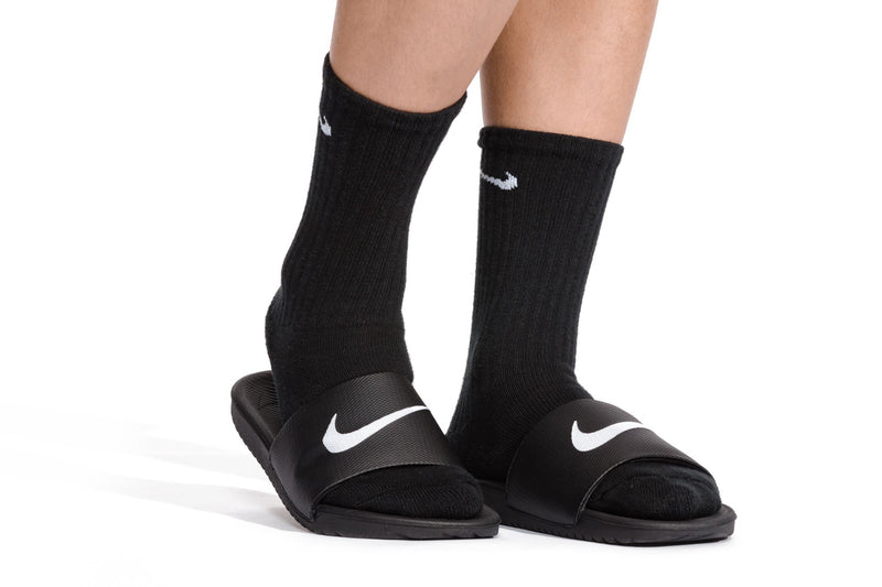 Kids black slide sandals worn with black socks, white Nike swoosh on straps