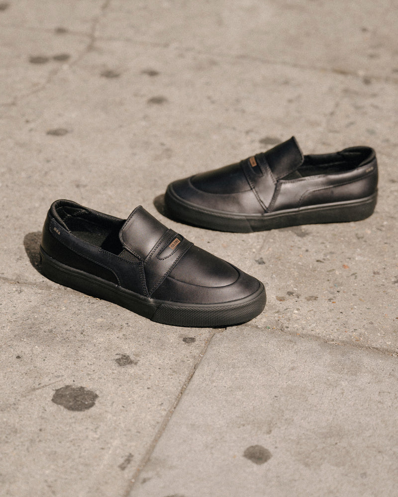 Liaizon Black Maalouf slip-on skate shoes in black leather photographed on a textured concrete surface.