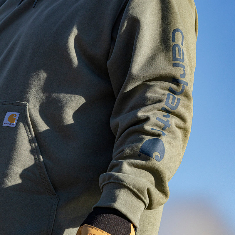 Dusty olive hoodie sleeve close-up with blue Carhartt-style graphic