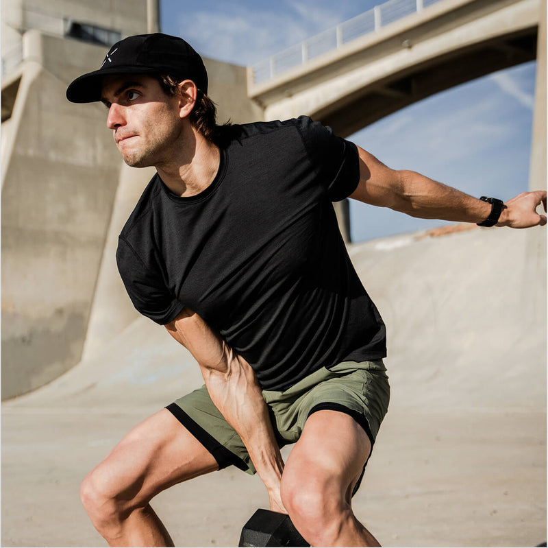 Man in ten thousand interval shirt outdoors working out with a bridge in the background