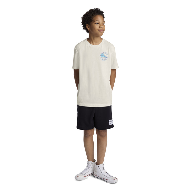 Youth off-white T-shirt worn by child, blue chest logo and black shorts pairing