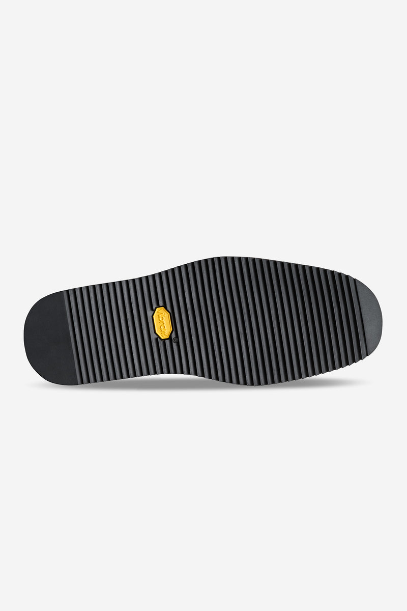 Bottom view of the oxblood mule showing a black ribbed Vibram sole with a yellow logo badge.