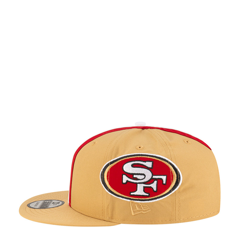 Tan baseball cap with large oval team logo patch and red underside bill edge