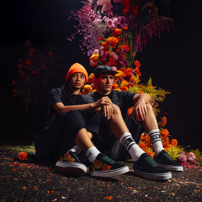 Pair of black low-top sneakers with marigold floral artwork, worn with white socks