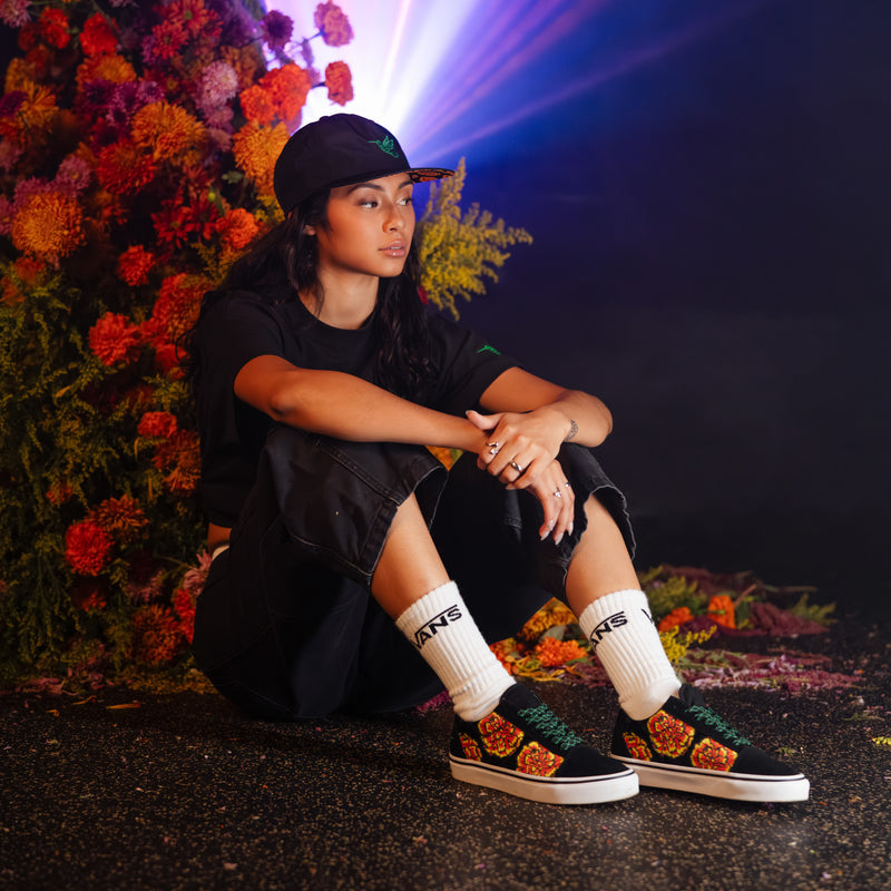 Black low-top sneakers with marigold floral print, green trim, and white socks