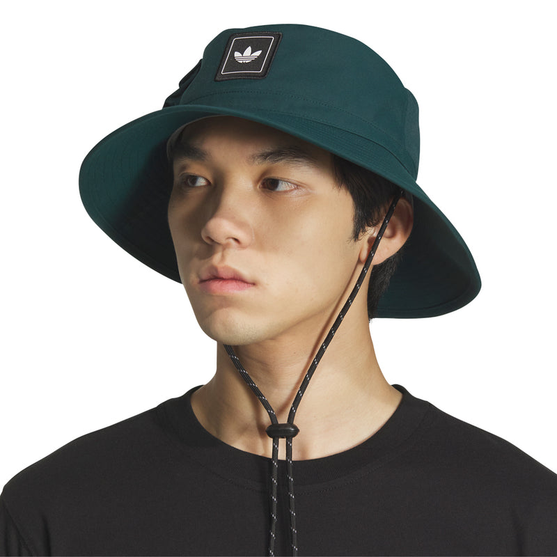 Dark green boonie hat with adidas trefoil patch and chin cord, worn by model