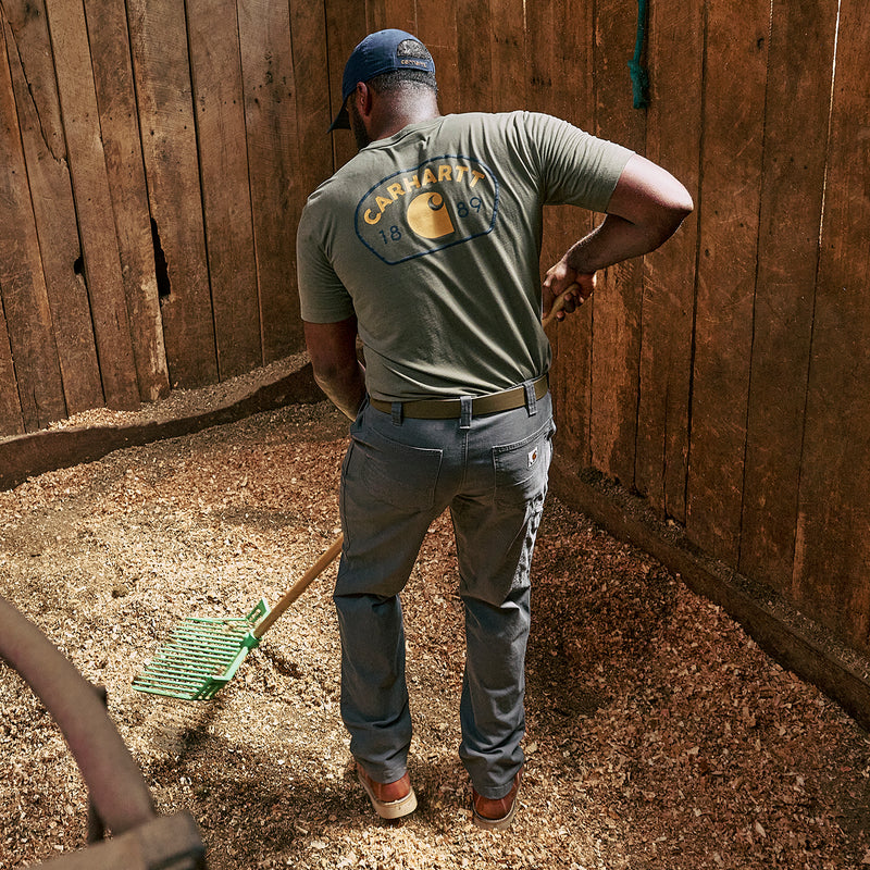 Men's relaxed straight dungaree pants in gravel gray, back view standing in work area.