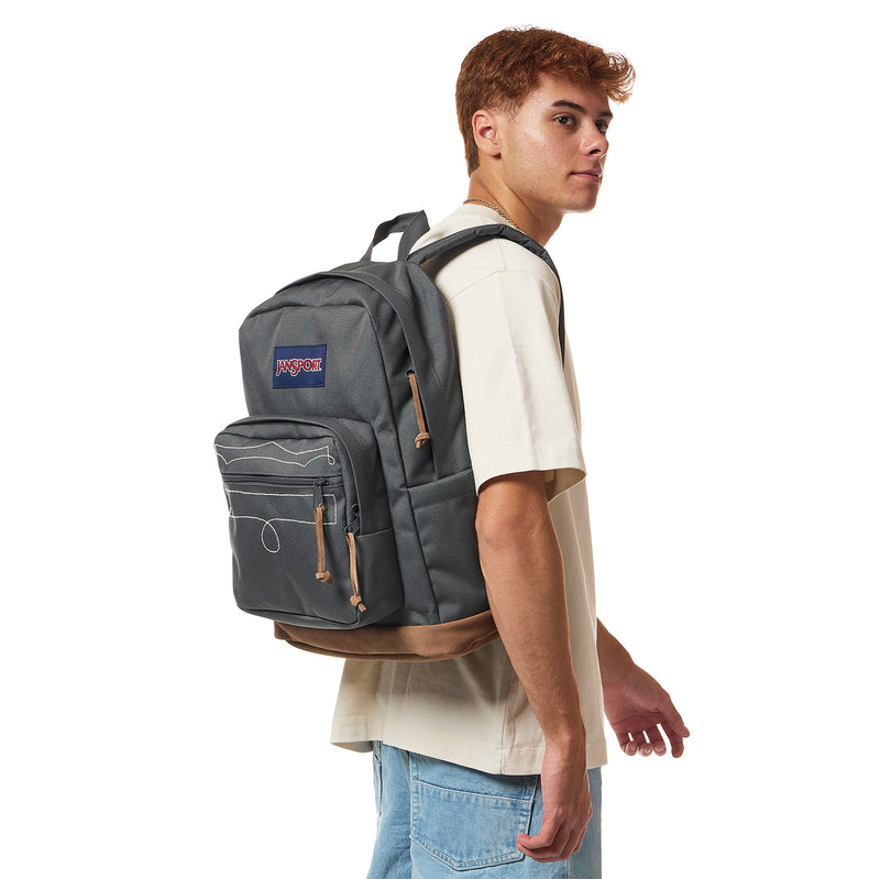 Gray JanSport backpack worn by model, side profile with front pocket and tan drawcord pulls.