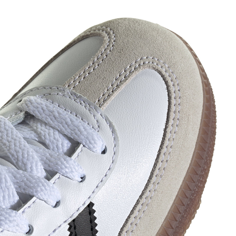 Kids white low-top sneaker close-up with laces, stitched overlays, and gum-brown sole