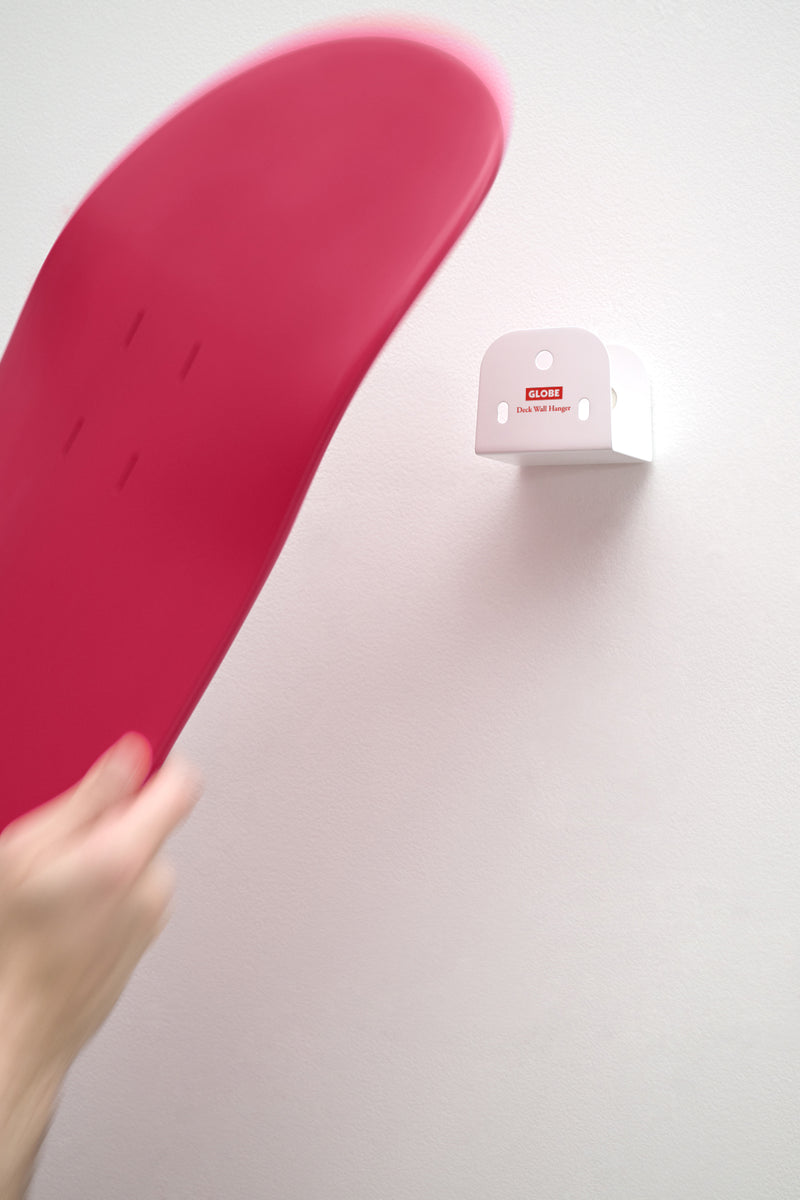 Pink skateboard being mounted on a white wall mounted deck hanger with clear acrylic bolts