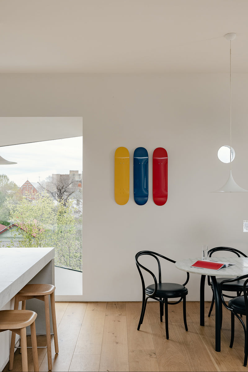 Three colored skateboard decks yellow blue and red mounted on a white wall beside a dining table