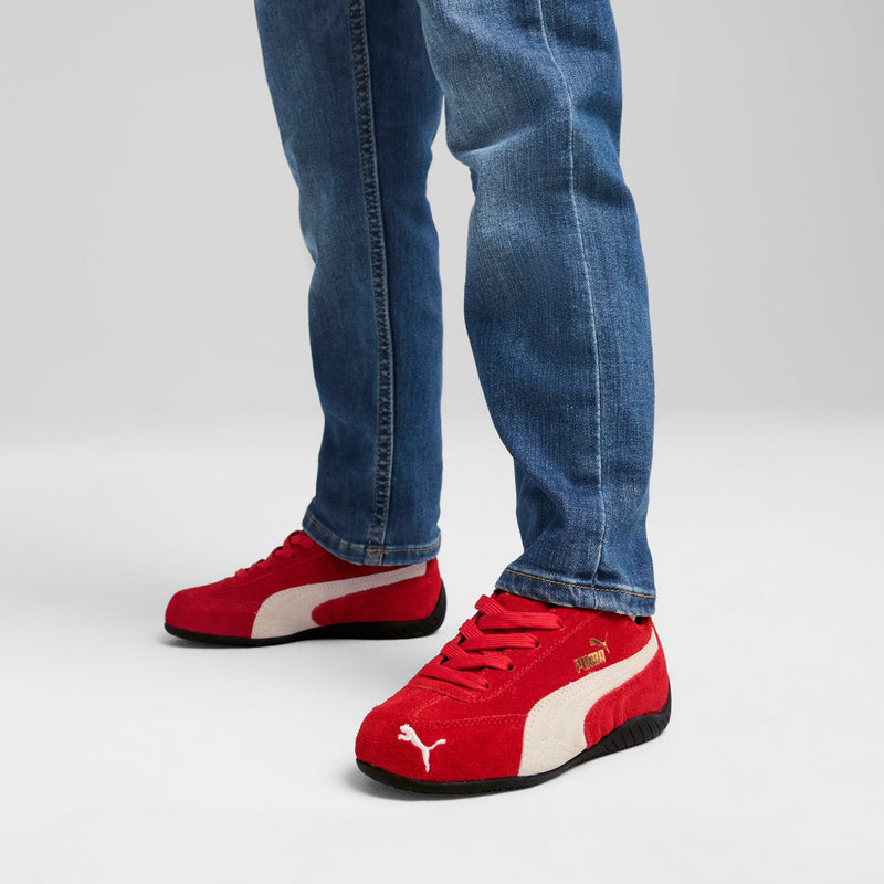 Kids red sneakers with white panels and black sole, worn with blue jeans
