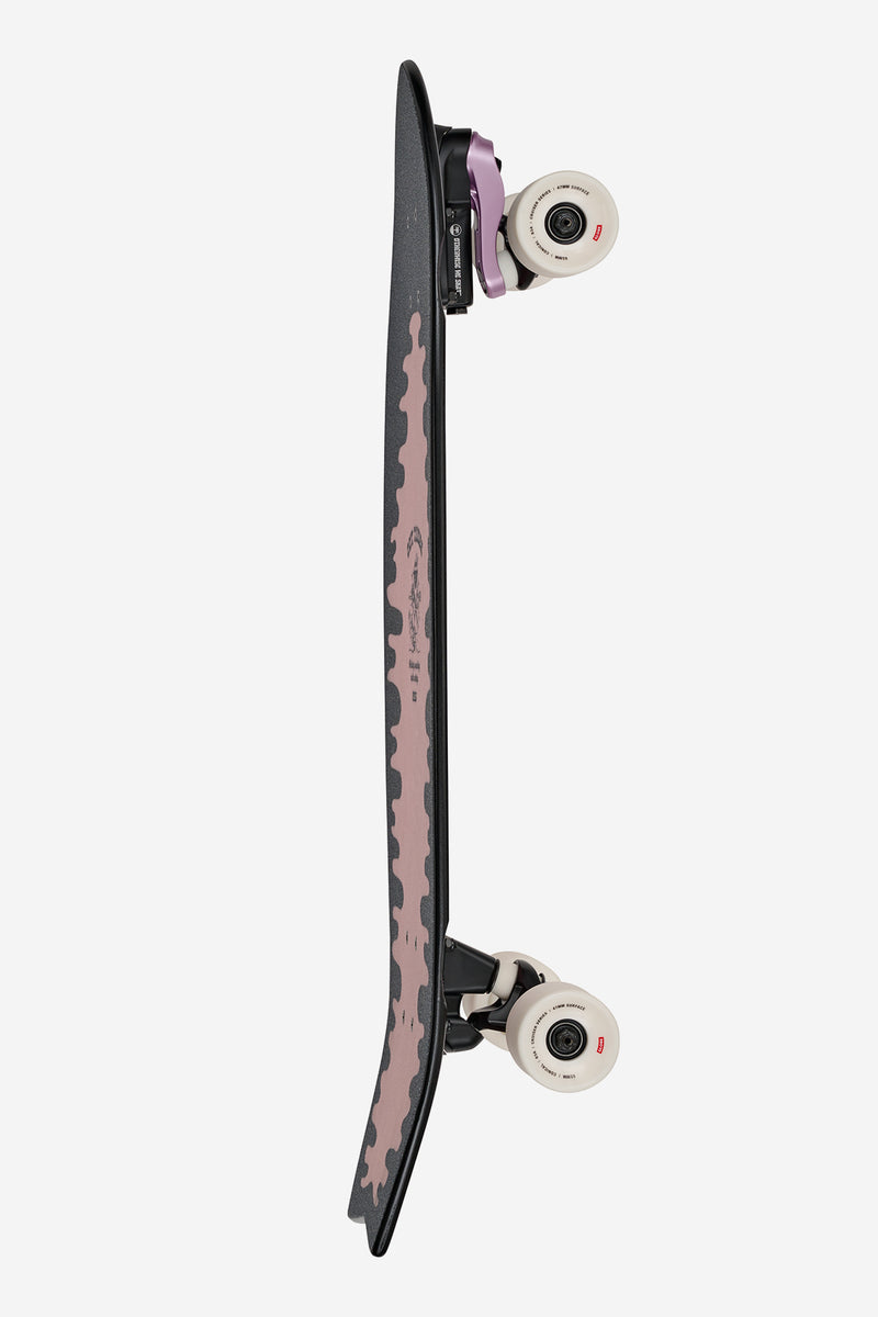 Side view of a 30 inch Sun City 2 Surf Skate Lazy Daisy with dark deck pink center graphic white wheels and purple trucks