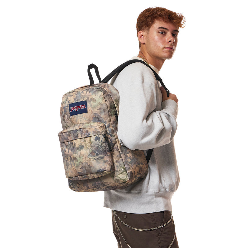 JanSport Superbreak Plus camo backpack worn by a person, side view with top handle