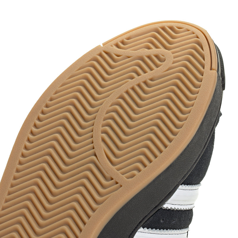 Close-up of gum rubber outsole with zigzag tread pattern on black sneaker.