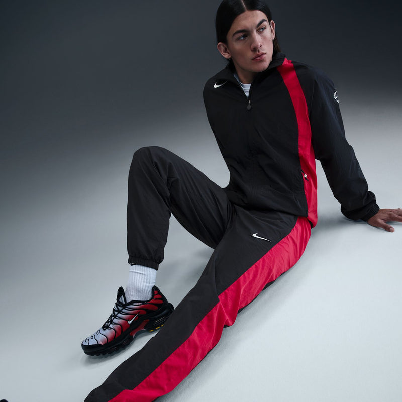 Men's black track pants with red diagonal side panel and Nike swoosh at knee