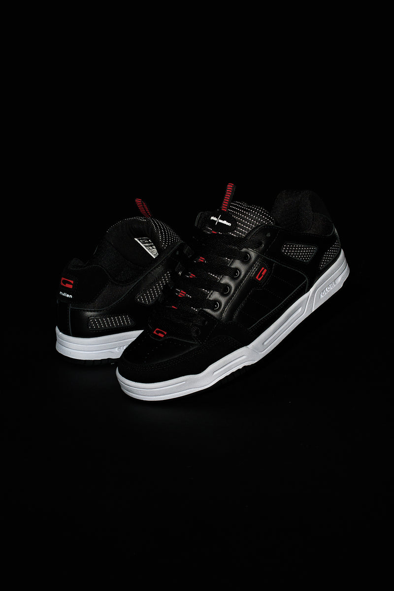 Pair of Tilt Prime black leather skate shoes on a black background with white midsoles and red details