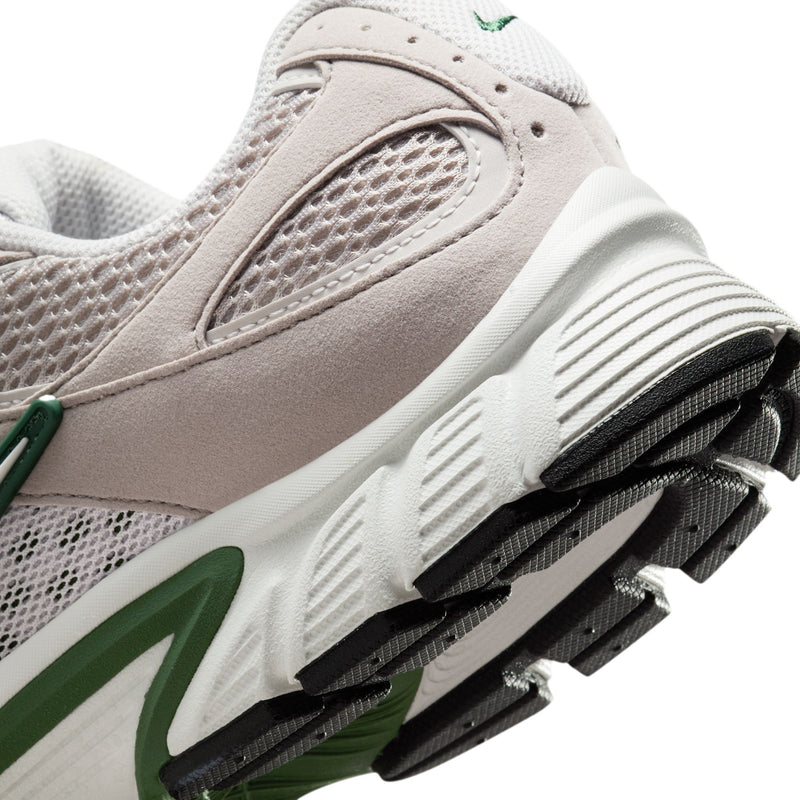 Close-up of light gray sneaker side with green swoosh and black traction pods