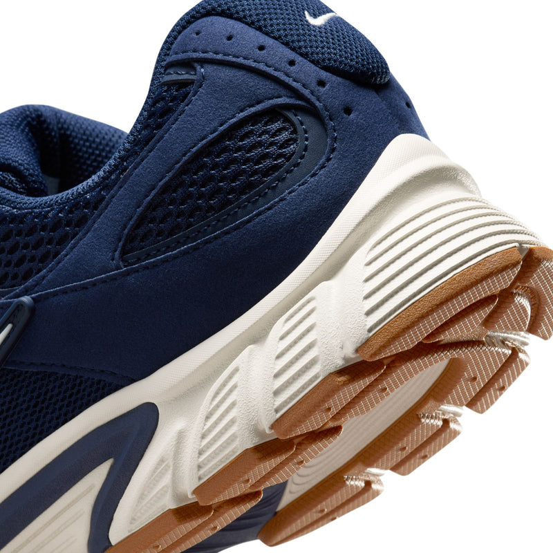 Close-up of navy sneaker side panel with white stripes and tan outsole edge
