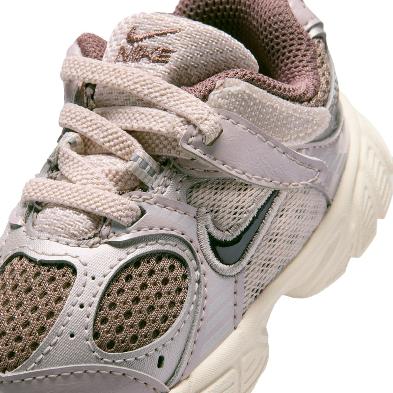 Toddler sneaker close-up: light taupe mesh, stitched overlays, laces, and green swoosh